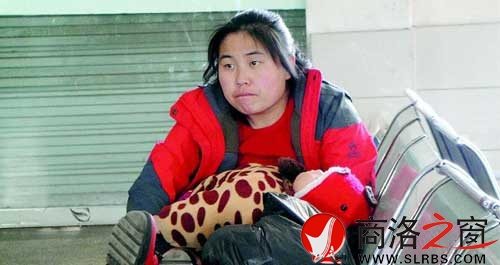 候車(chē)廳里，一位母親抱著睡著的孩子發(fā)呆